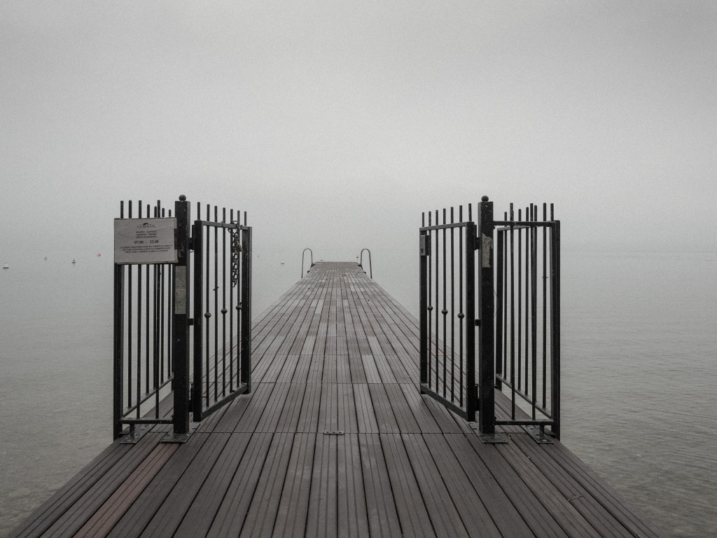 Photo of a pier with an open gate in the mist on Lake Garda, Bardolino, Italy.
