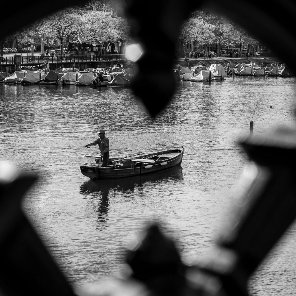 Fisherman in boat on Limmat river framed by railings, Zurich black and white photography