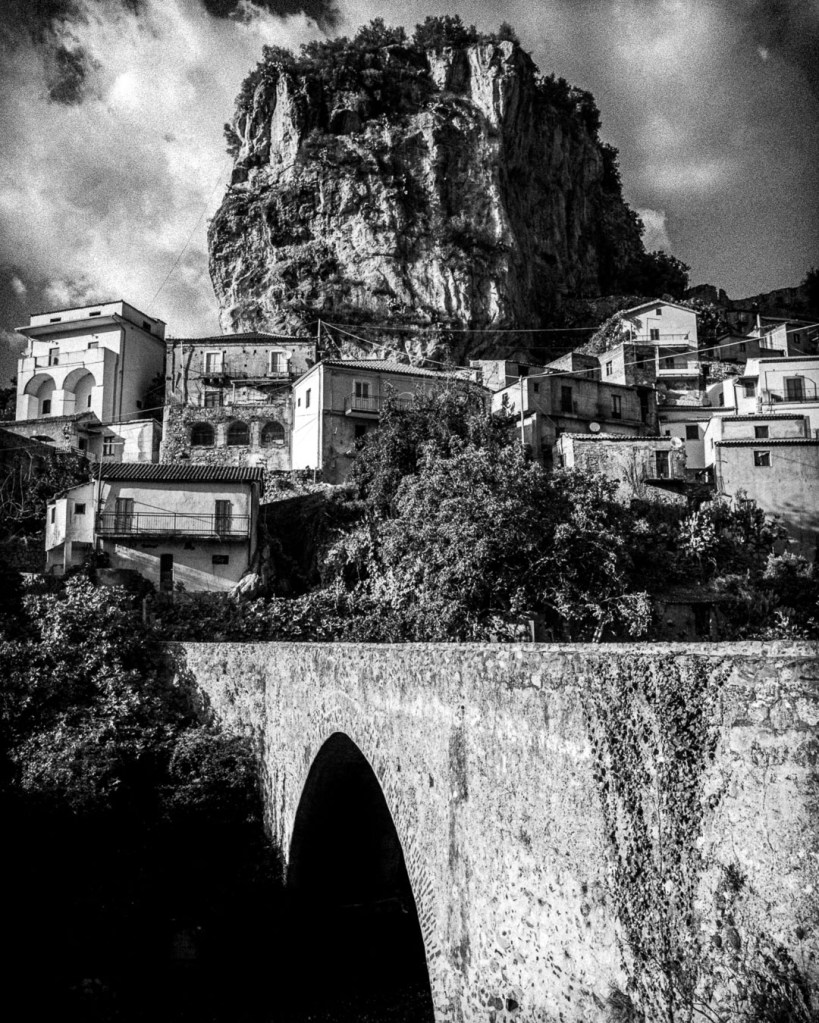 Black-and-white photo of Palizzi Superiore, Calabria, showing a hillside village with tiled roofs and stone buildings