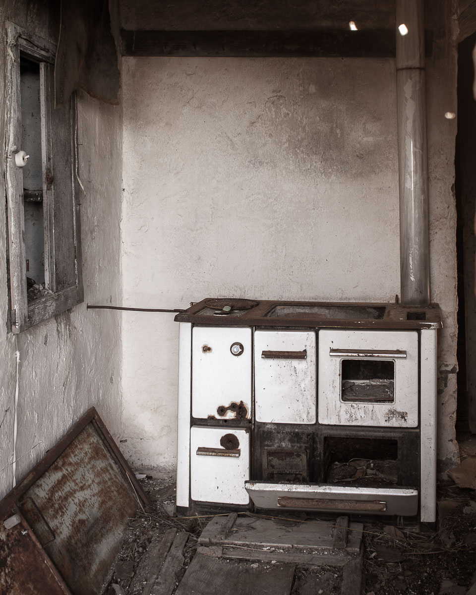 Corroded vintage stove in derelict Ferruzzano Superiore home with peeling walls and broken window, Calabria.