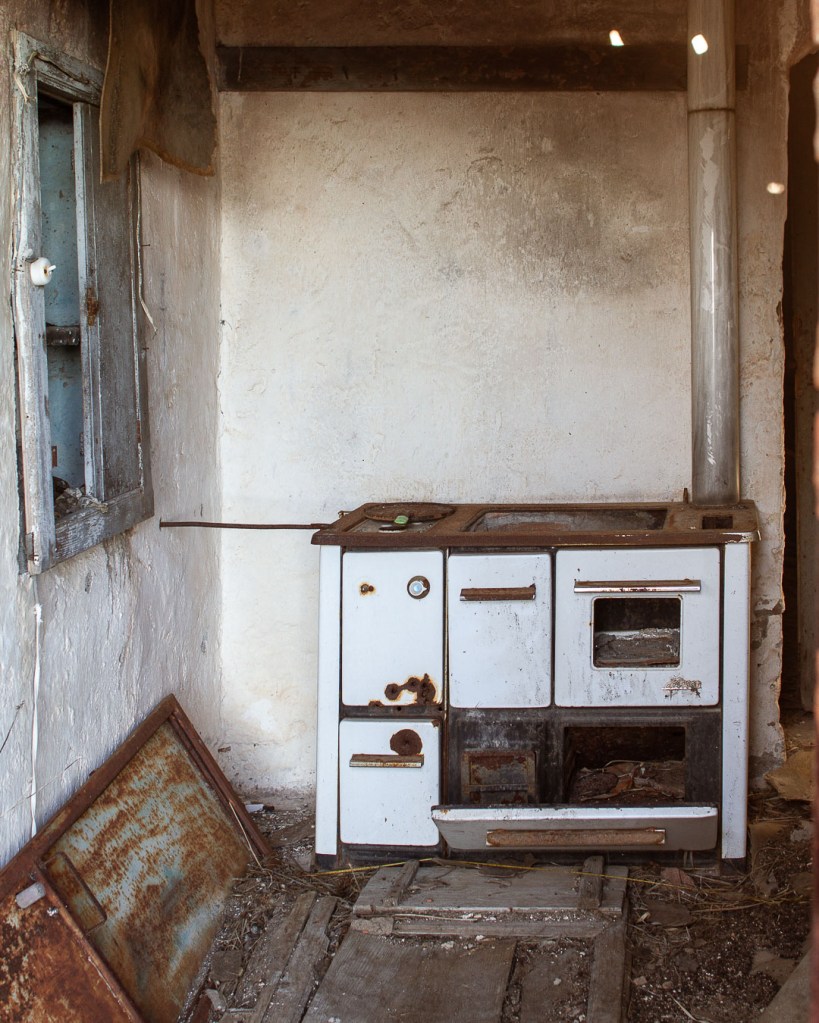 Corroded vintage stove in derelict Ferruzzano Superiore home with peeling walls and broken window, Calabria.