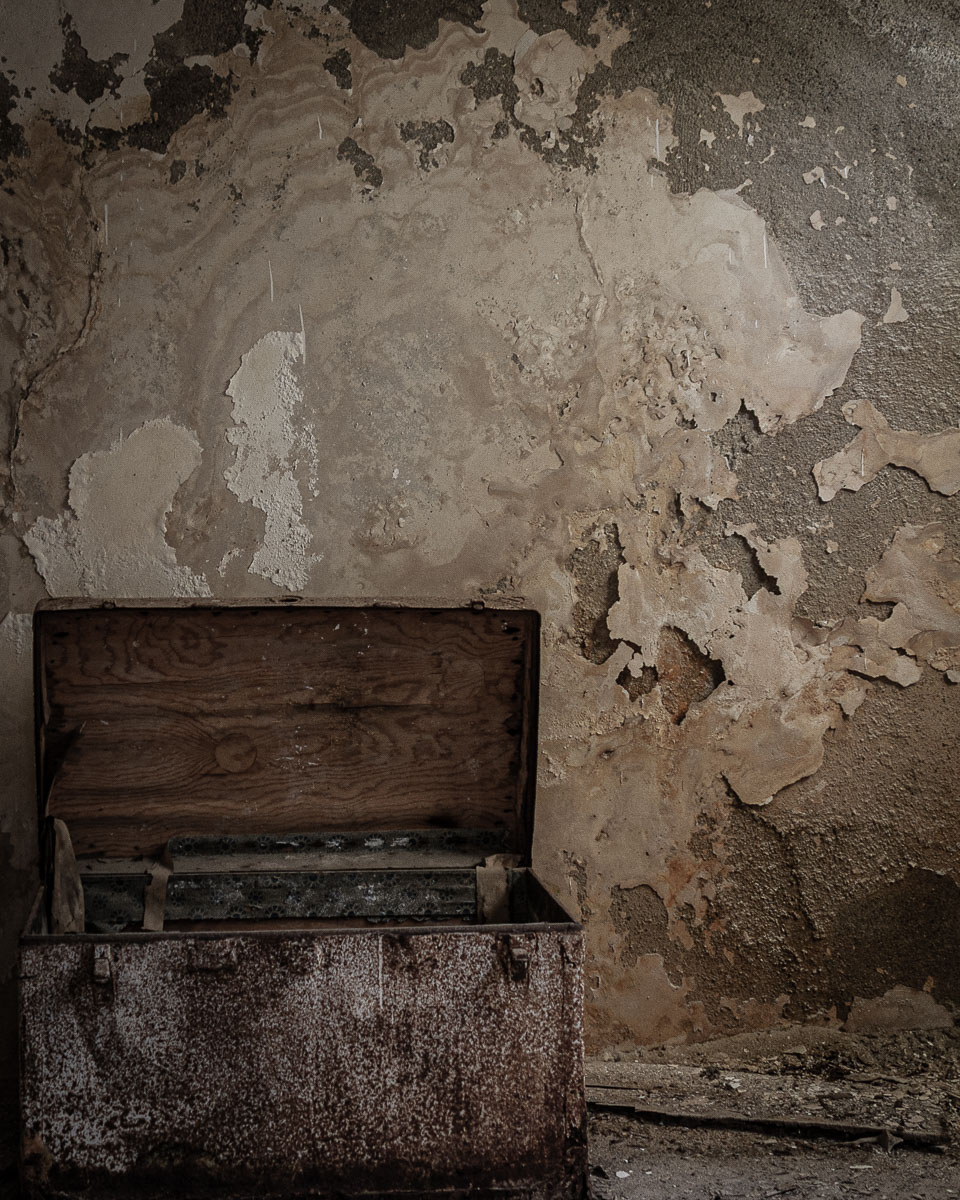 Open rusted metal chest in decayed room with peeling plaster and exposed textures in Ferruzzano Superiore, Calabria.