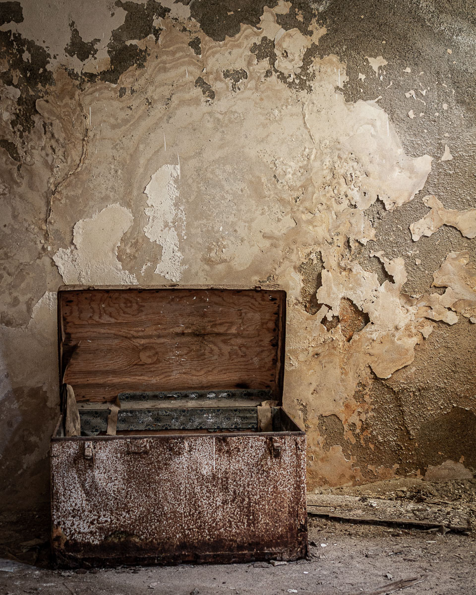 Open rusted metal chest in decayed room with peeling plaster and exposed textures in Ferruzzano Superiore, Calabria.