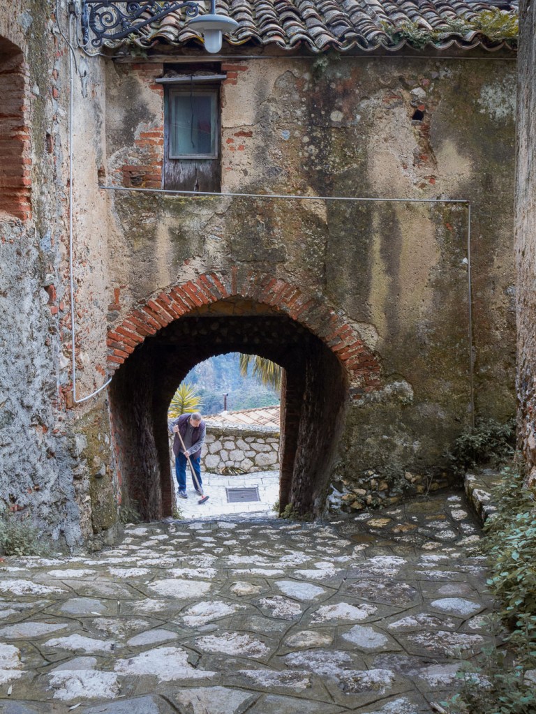 Man sweeping under a stone arch in a village alley, Staiti, Calabria