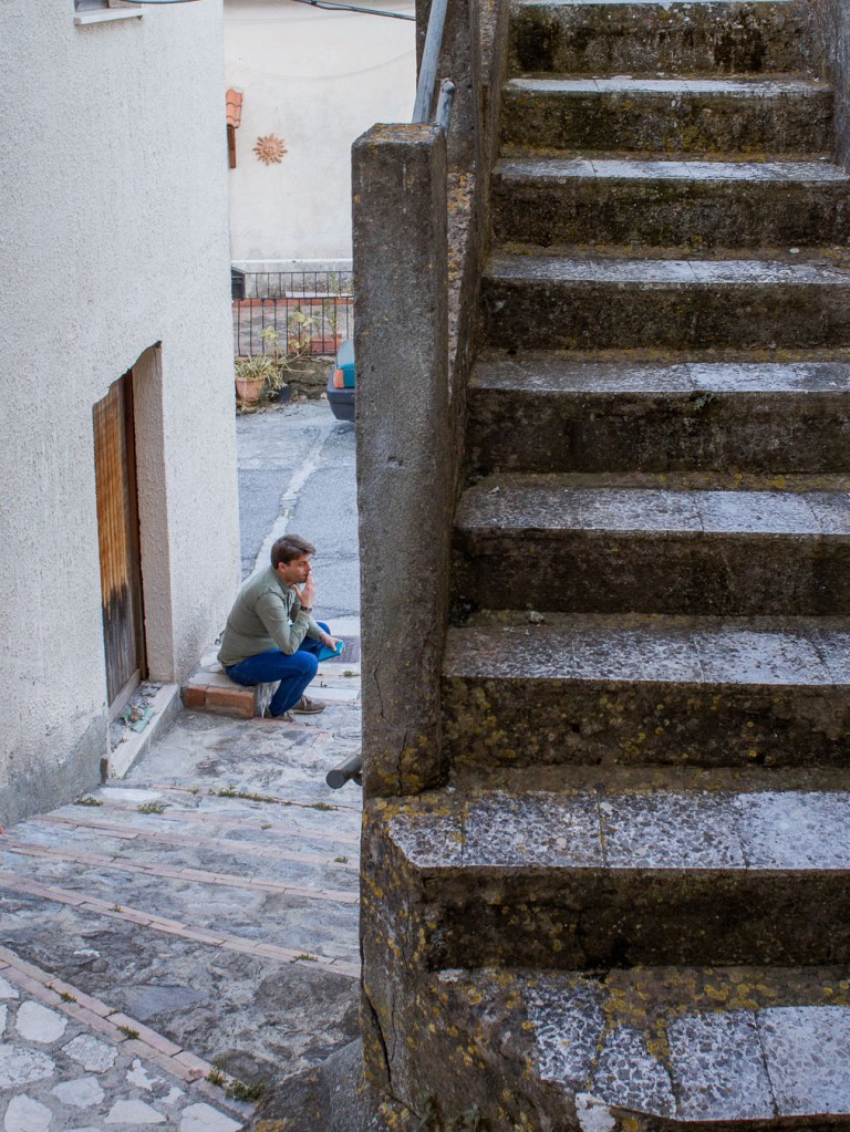 Man sitting in a village alley framed by stone staircase, Palizzi Superiore, Calabria