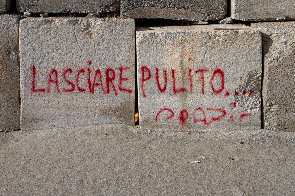 Red spray-painted words "Lasciare pulito grazie" on concrete blocks, San Pasquale, Bova Marina