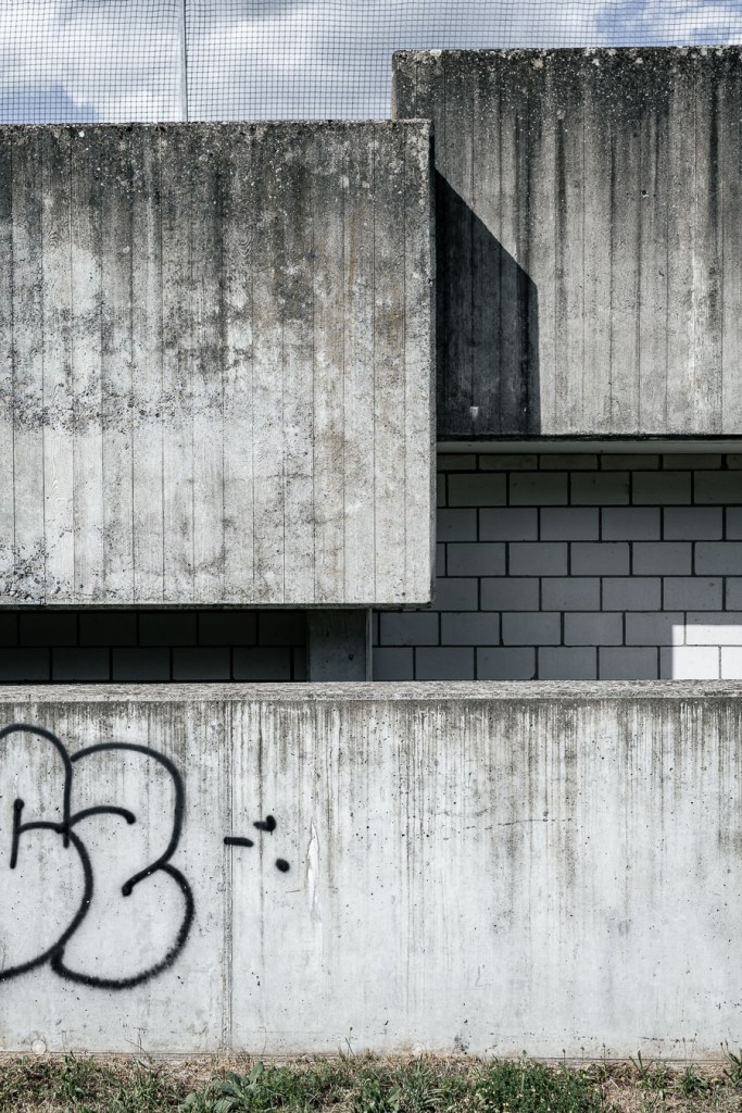 Layered concrete architectural volumes with a sharp diagonal shadow and black spray-painted marks on the lower wall, Bülach, Switzerland