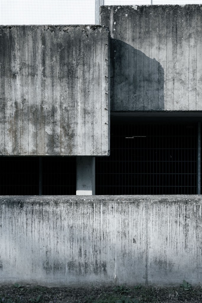 Layered concrete architectural volumes with a sharp diagonal shadow and black spray-painted marks on the lower wall, Bülach, Switzerland
