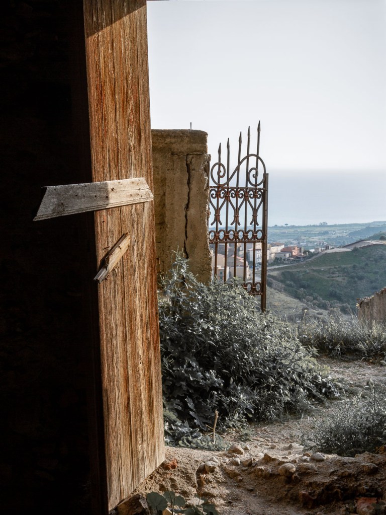 Abandoned wooden door and ornate iron gate overlooking coastal landscape, Pentedattilo, Calabria