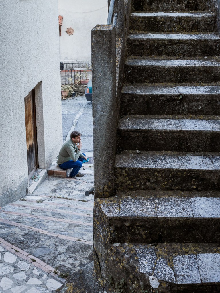 Man sitting in a village alley framed by stone staircase, Palizzi Superiore, Calabria