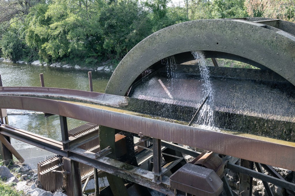 Close view of a water wheel: water falling from a metal flume onto the blades.